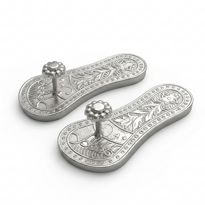 A pair of pure silver raised traditional Khadau footwear featuring detailed floral patterns, shown against a plain light background.
