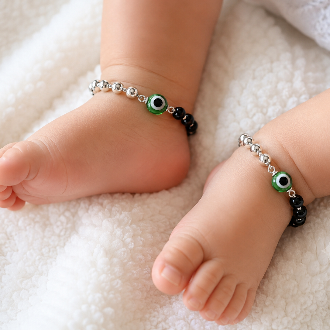 Baby feet wearing anklets with green eye design on a soft surface