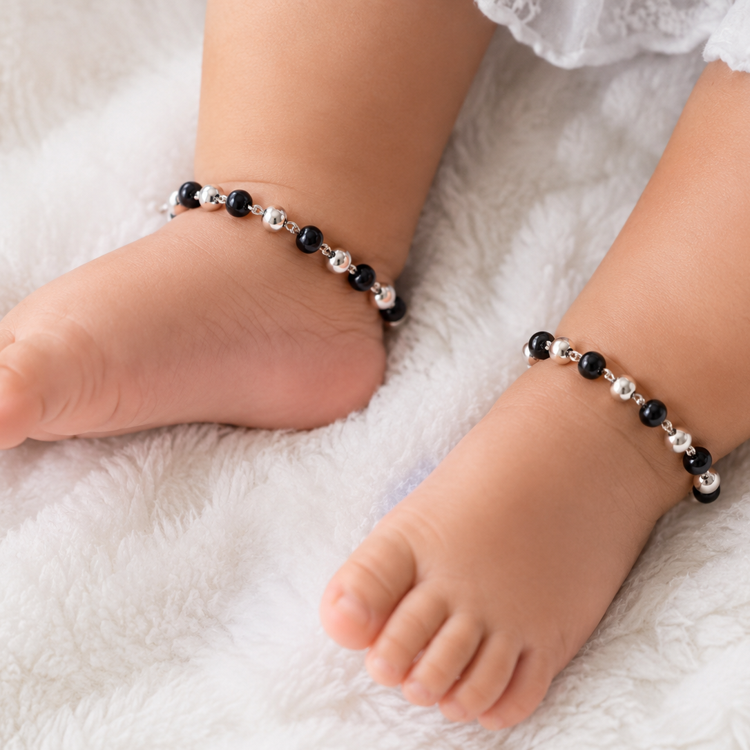 Baby feet wearing beaded anklets on a soft white surface