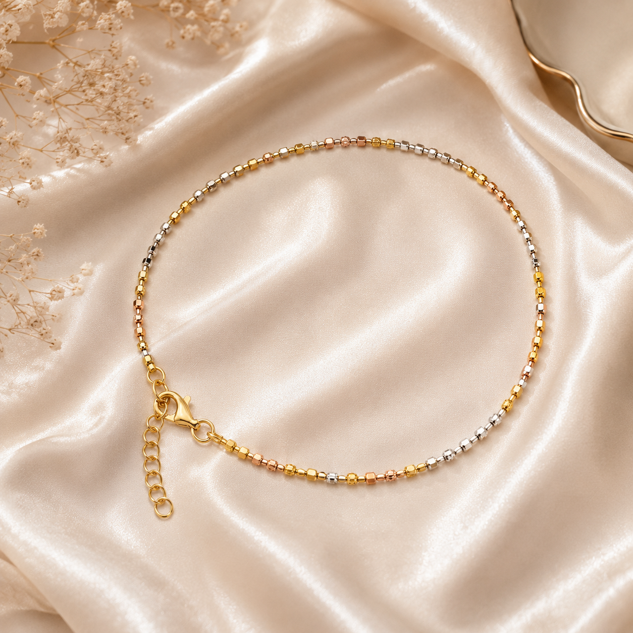 Gold anklet on a satin surface with dried flowers