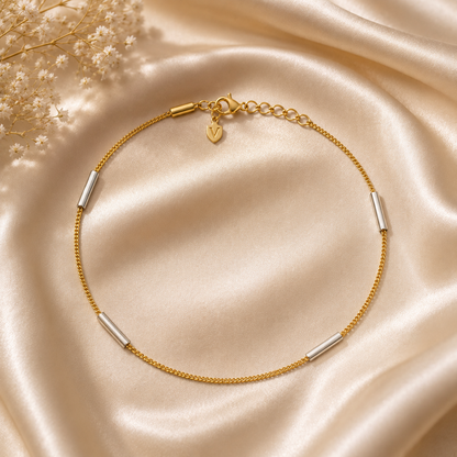 Gold bracelet with silver cylindrical beads on a beige satin background
