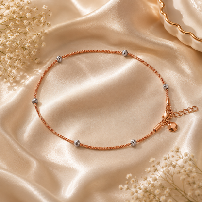 Rose gold anklet with small charms on a beige satin background