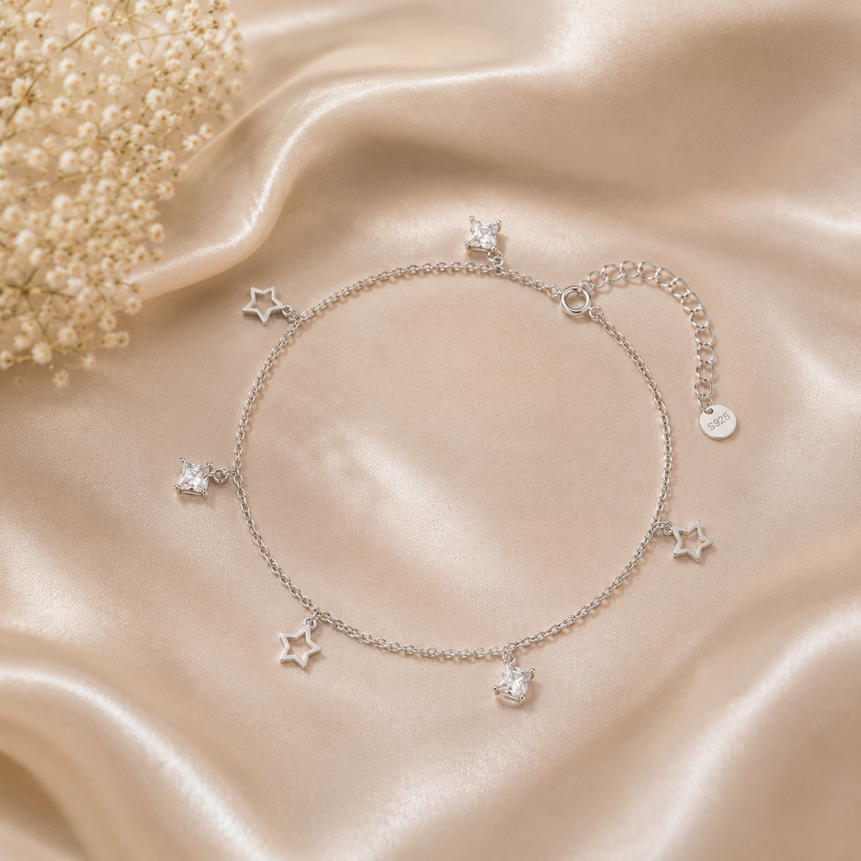 Silver anklet with star charms on a soft beige fabric background
