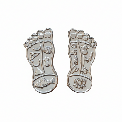 Silver foot-shaped pendants with engraved designs on a white background