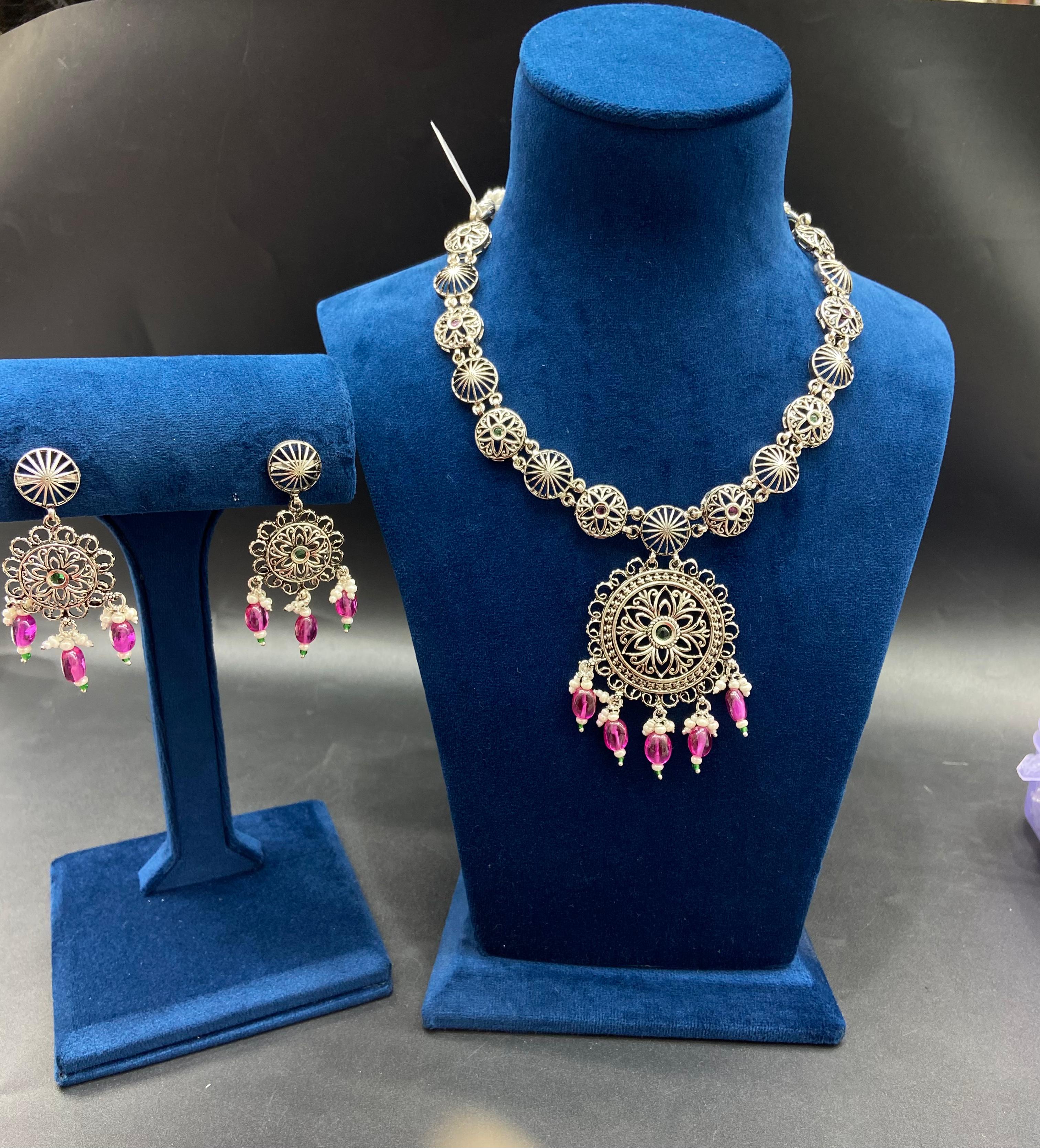 Vintage Silver Necklace Set featuring a deeply oxidized antique patina medallion with radial filigree, kundan-style stone arrangements, and matching drop earrings on a premium display stand by Rivansh.